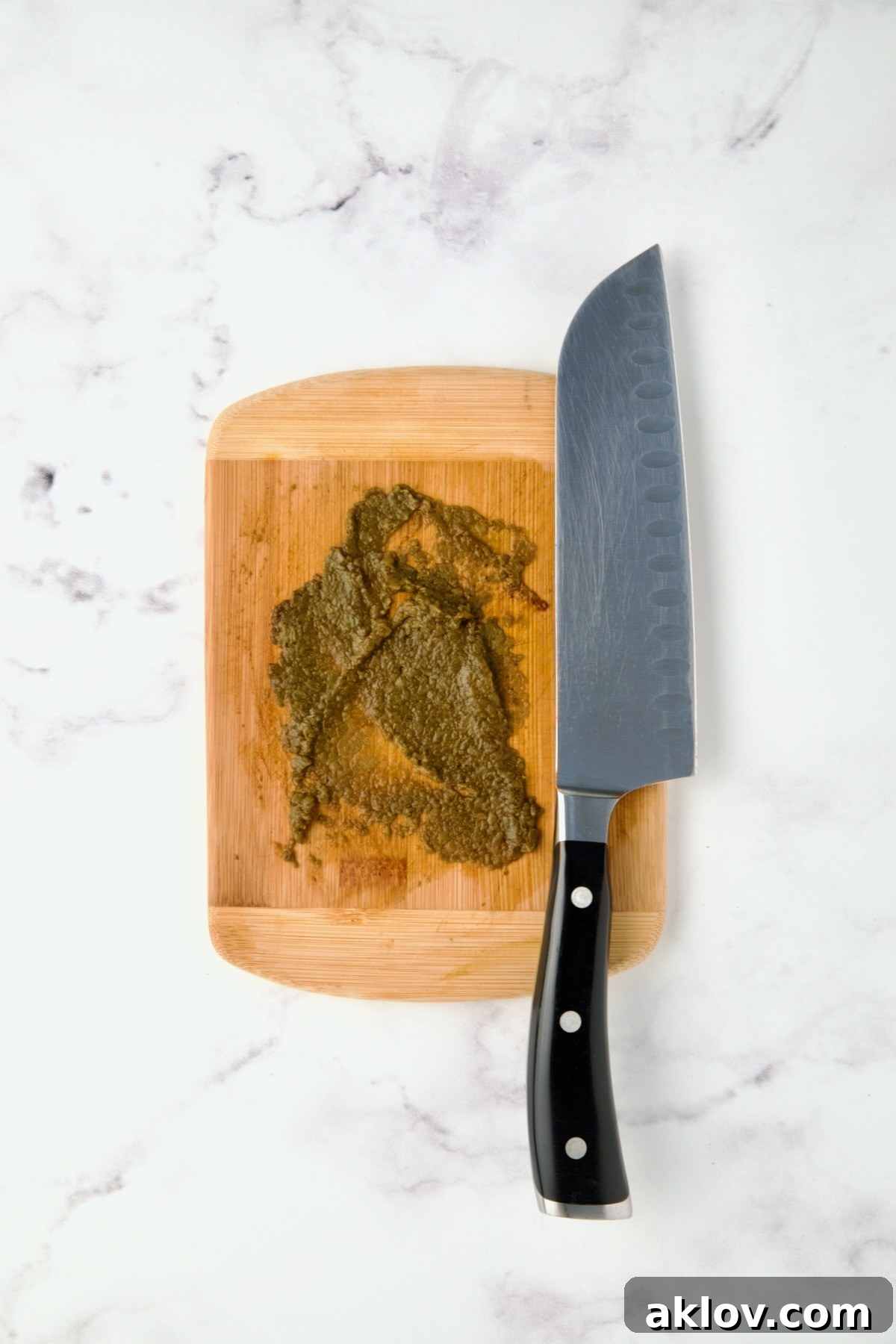 Mashed chipotle chiles on wood cutting board with chef knife.