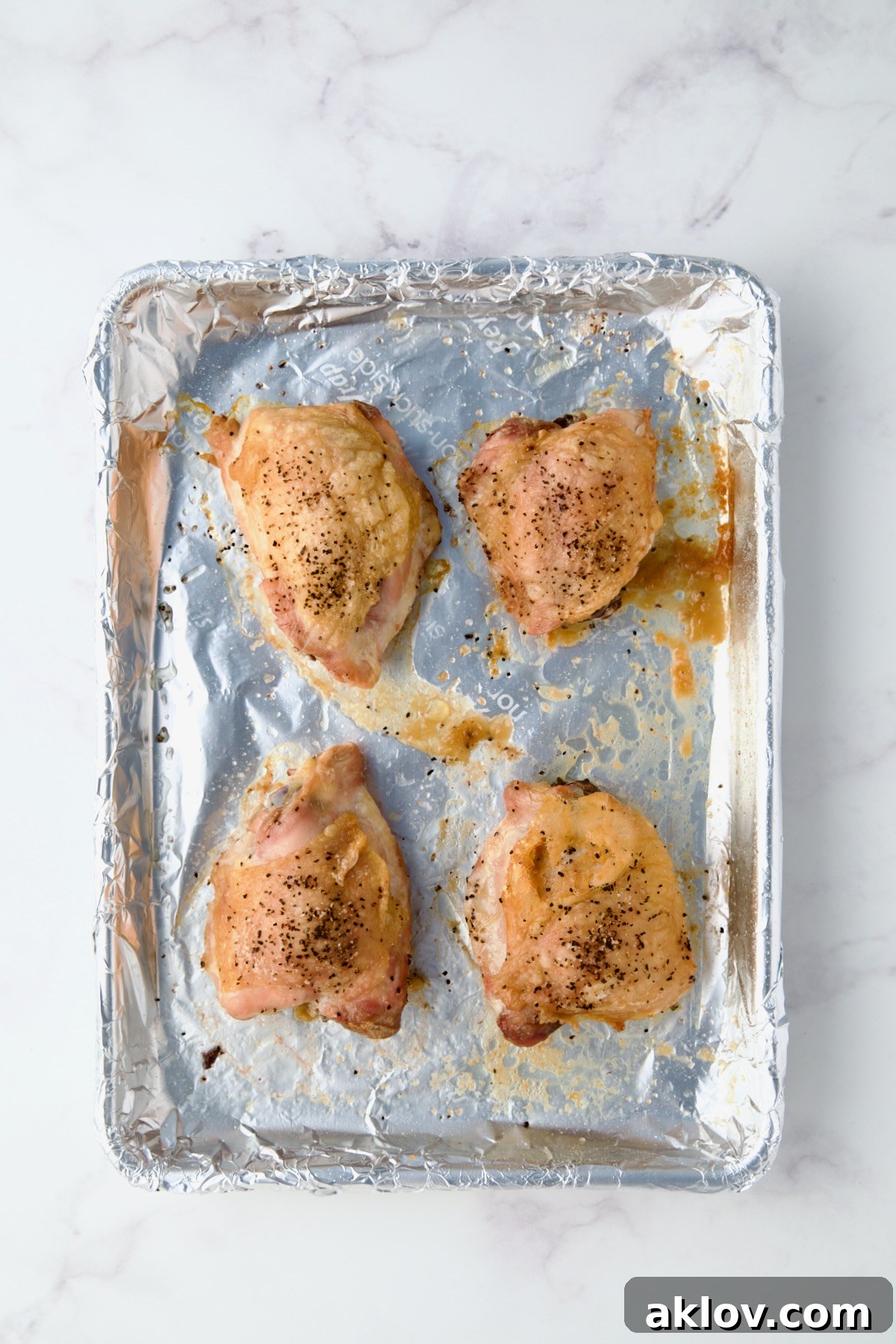 Four baked chicken thighs on aluminum foil-lined baking sheet.