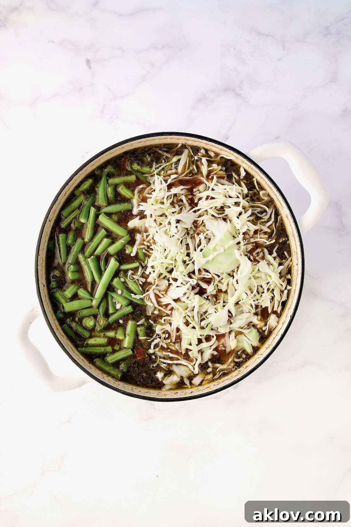 Green beans and cabbage added to the simmering soup in a white Dutch oven.