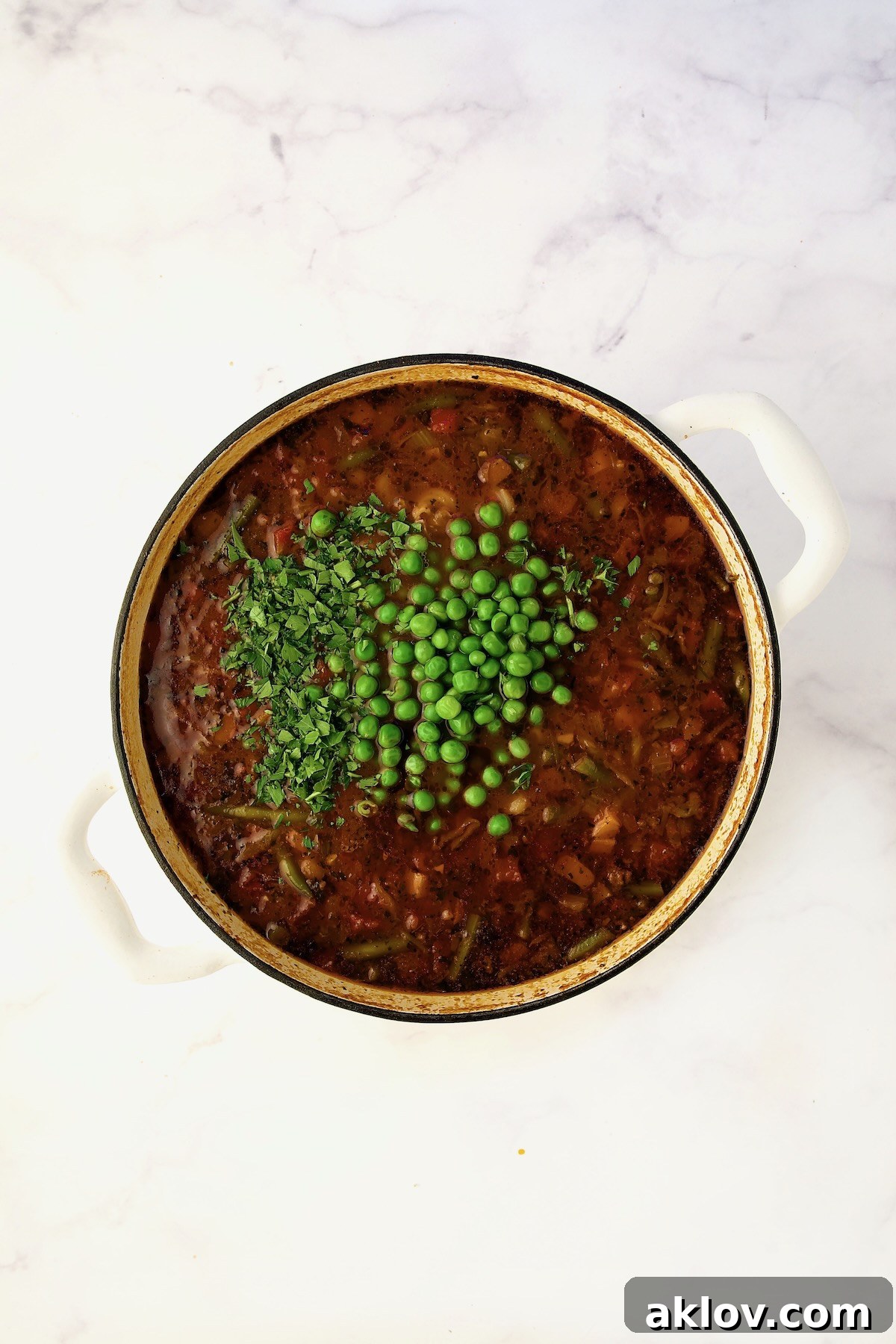 Peas and parsley added to the soup in process in a white Dutch oven.