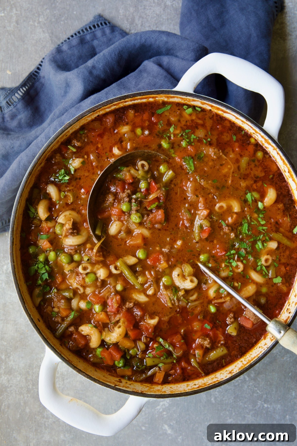 Finished Hamburger Vegetable Soup in a white Dutch oven with a soup ladle and a blue napkin.
