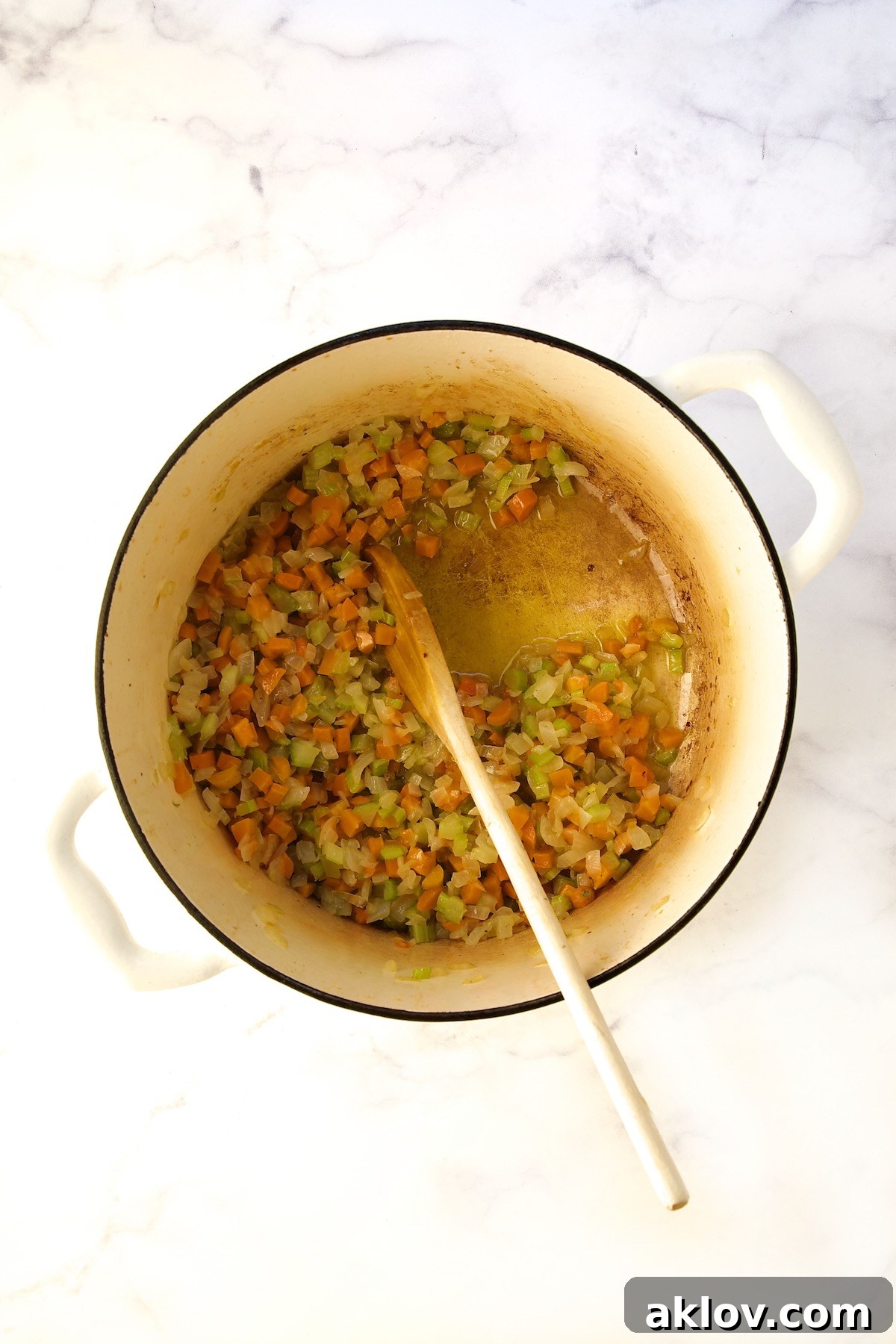 Sautéed onions, carrots, and celery in a white Dutch oven with a wooden spoon.