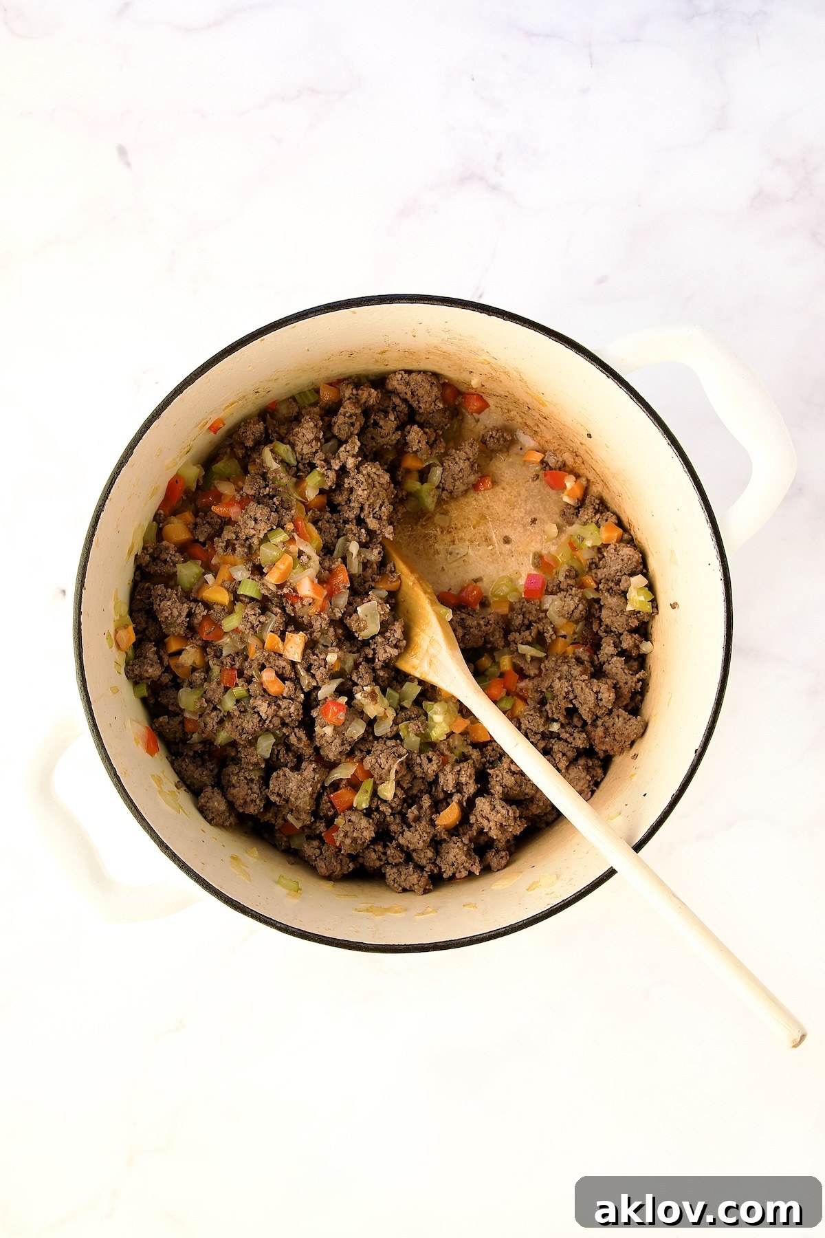 Ground beef reintroduced to the cooked vegetables and being stirred with a wooden spoon.