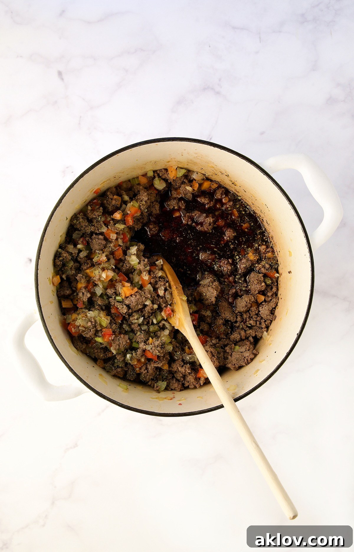Red wine added to the ground beef and vegetable mixture, being stirred.