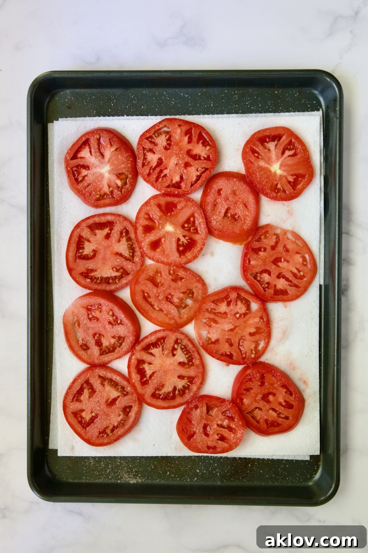 Sliced tomatoes draining on paper towel-lined rimmed baking sheet.