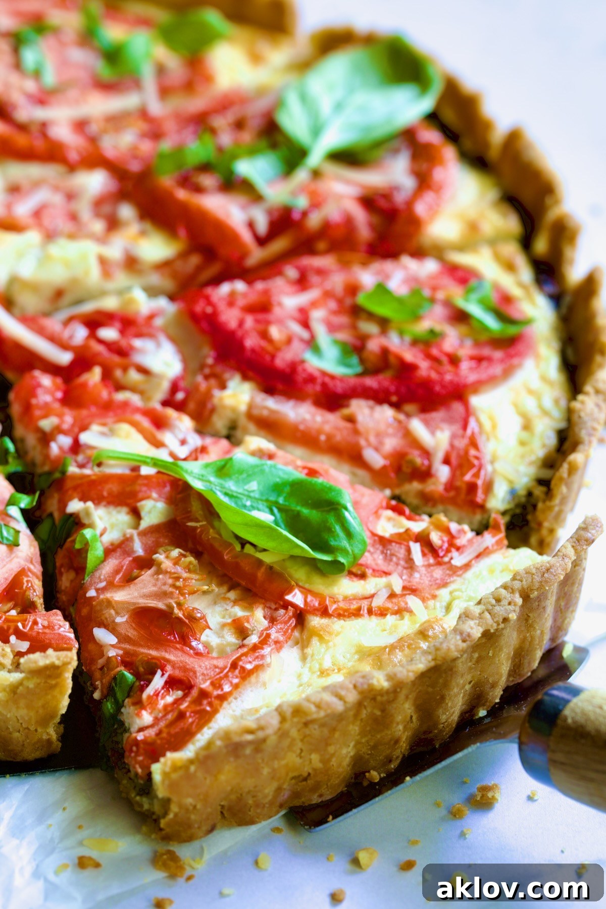 Tomato Tart with Ricotta and Cheese garnished with fresh basil leaves cut into wedges with pie server picking up a piece.