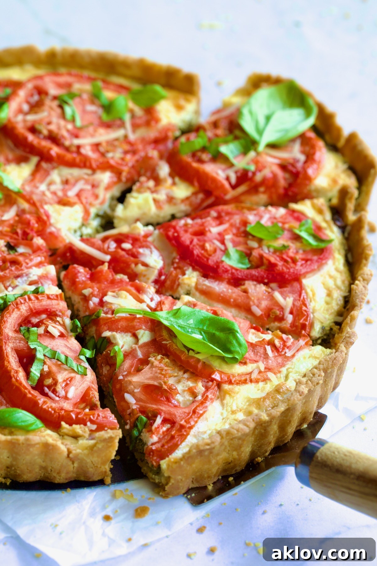 Tomato Tart with Ricotta and Cheese garnished with fresh basil leaves cut into wedges with pie server picking up a piece.