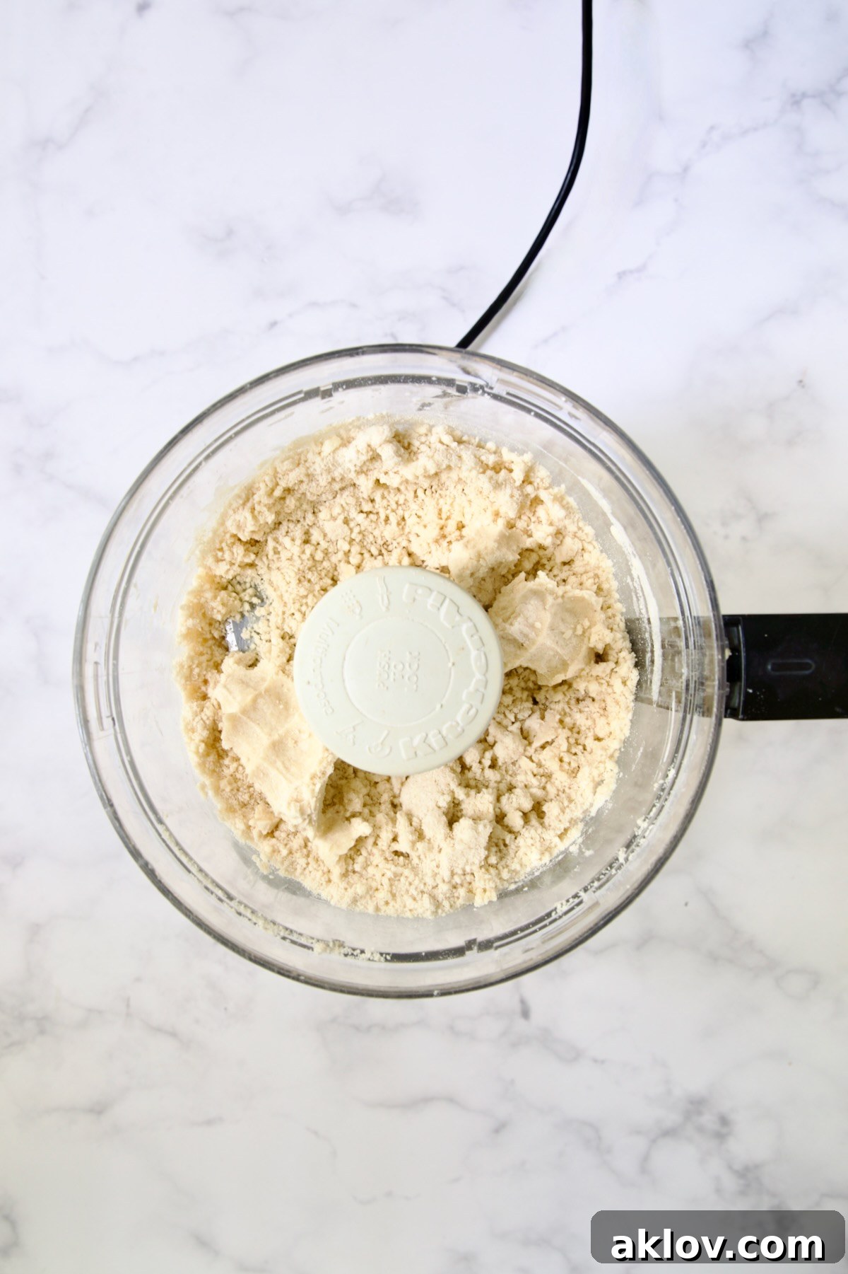 Butter cubes, flour, salt and pepper in bowl of food processor with ice water added demonstrating how it holds together.