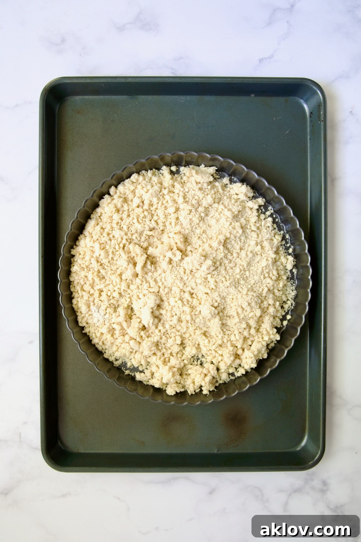 Tart crust dough in pan on rimmed sheet pan before being spread into tart pan.