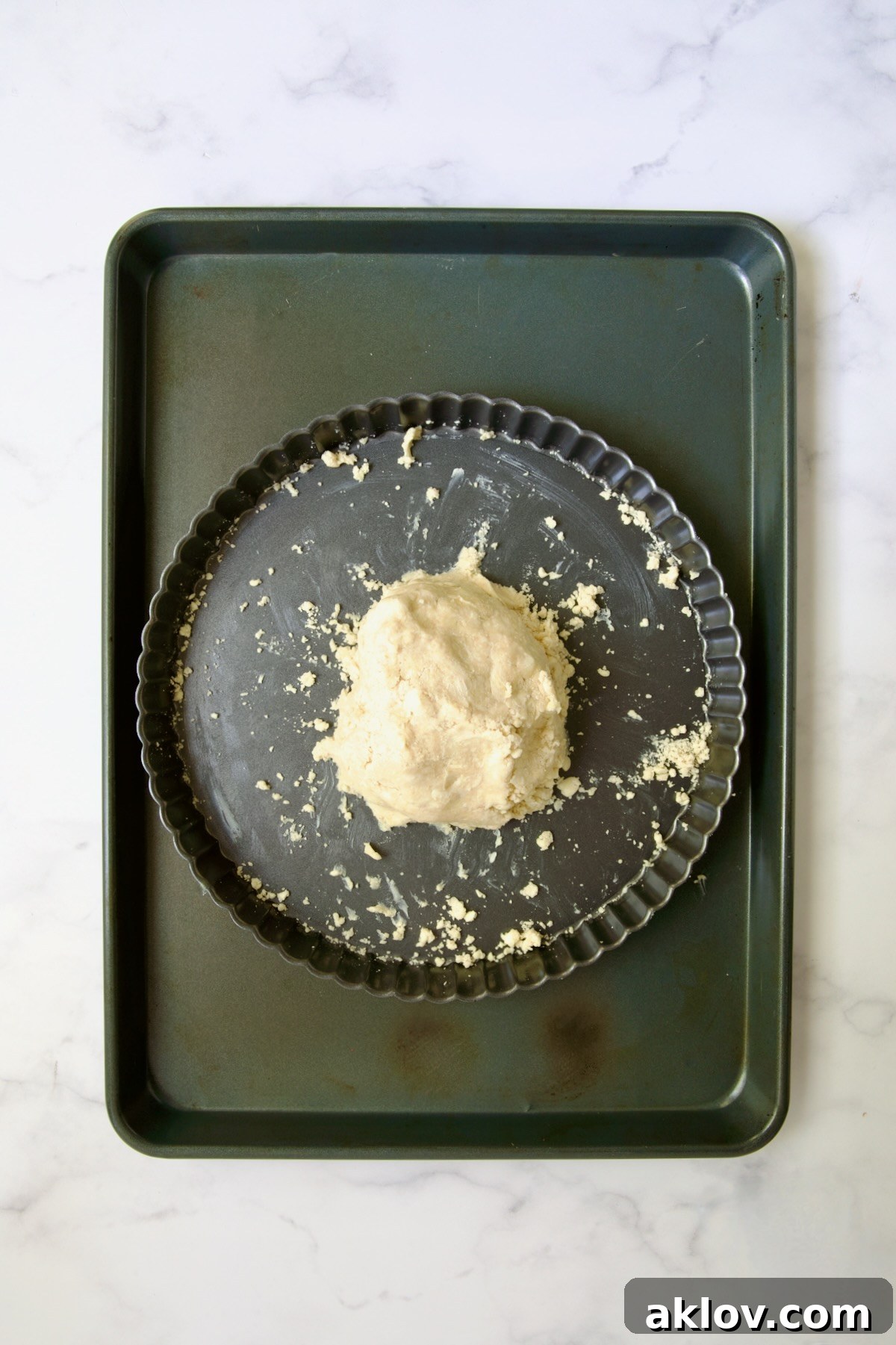 Tart dough gathered into a ball in tart pan on rimmed sheet pan.