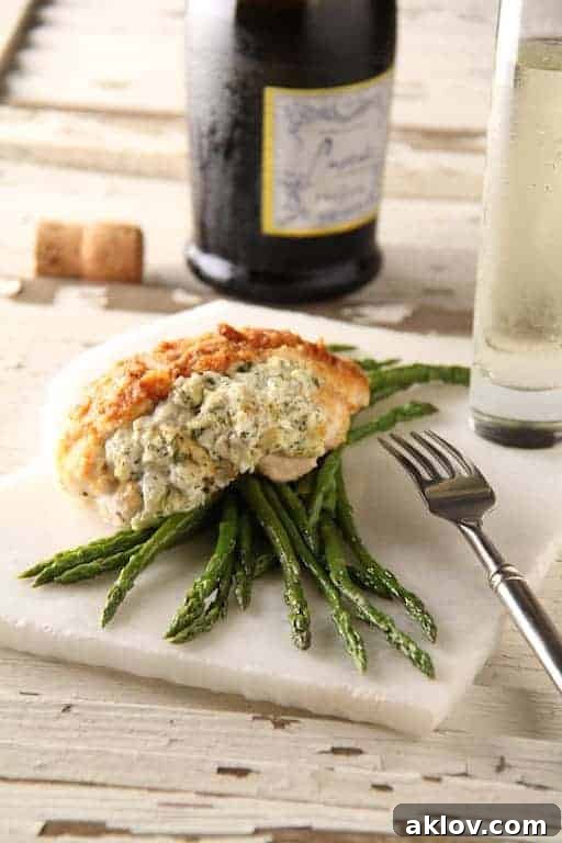 A single, perfectly portioned serving of Crab-Stuffed Chicken Breast, gracefully nestled over a bed of vibrant asparagus on a sleek white marble slab.