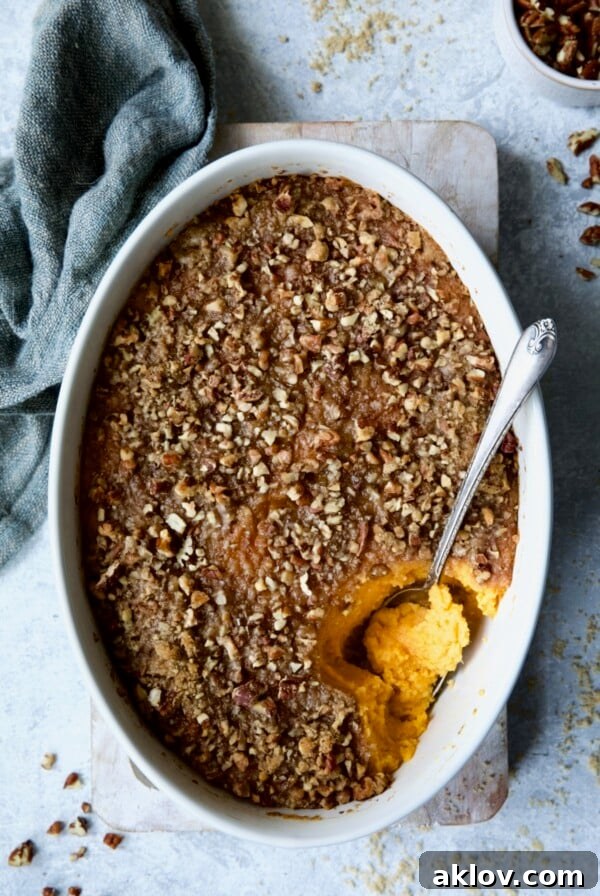 A golden-baked Sweet Potato Souffle in an oval baking dish, with a serving spoon poised to scoop out a fluffy portion.