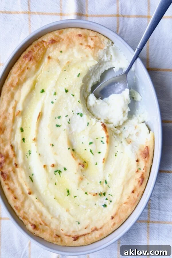 Creamy Twice-Baked Mashed Potatoes served in a white oval baking dish, with a serving spoon poised to dish out a portion.