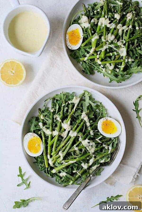 Two generous servings of Arugula, Egg, and Asparagus Salad with Creamy Lemon Vinaigrette, presented beautifully in elegant white bowls.