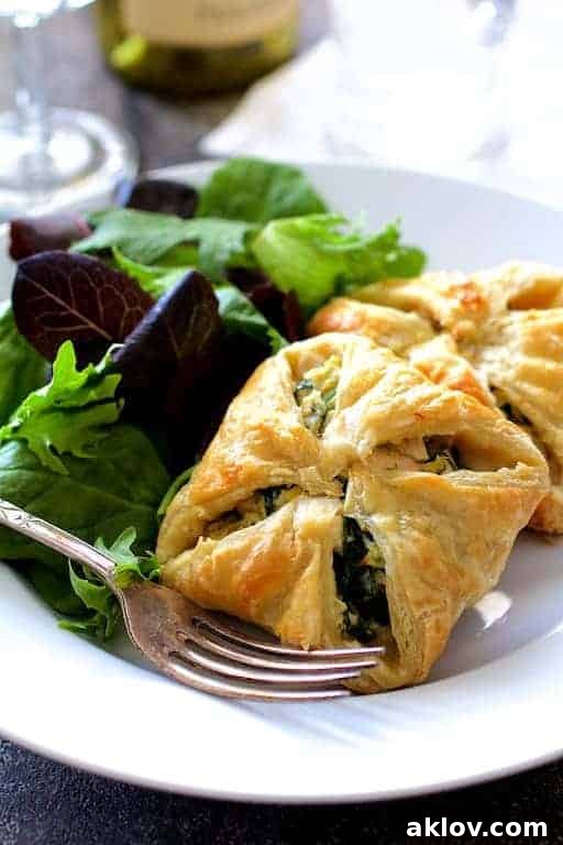 Two golden-brown Chicken Spinach and Artichoke Puff Pastry Parcels served on a white plate with fresh salad greens and a fork.