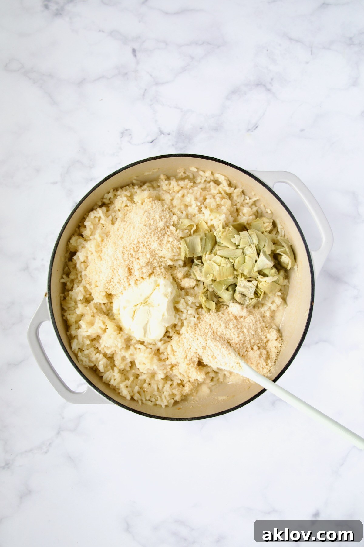 Parmesan cheese, mascarpone and artichokes added to cooked risotto in white enamel cast iron skillet.