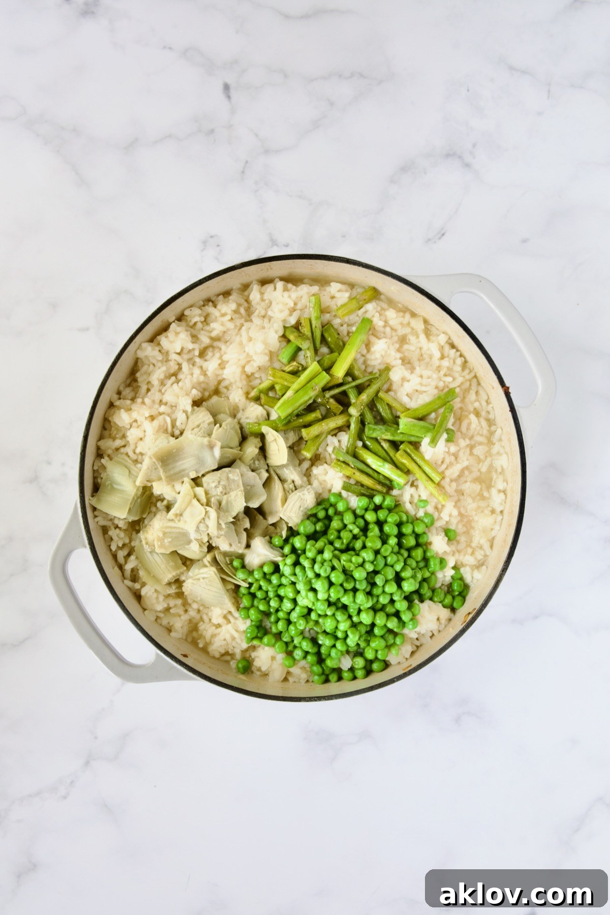 Asparagus stems, peas and artichoke hearts added to cooked risotto in white enamel cast iron skillet.