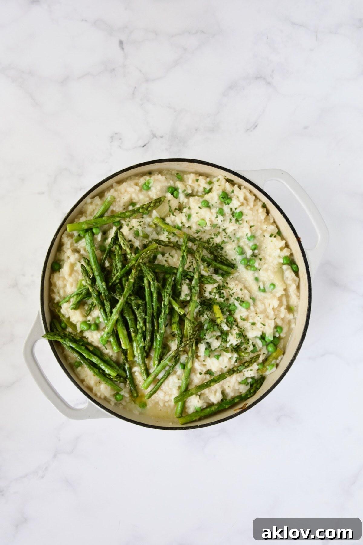 Cooked risotto topped with asparagus tips in white enamel cast iron skillet.