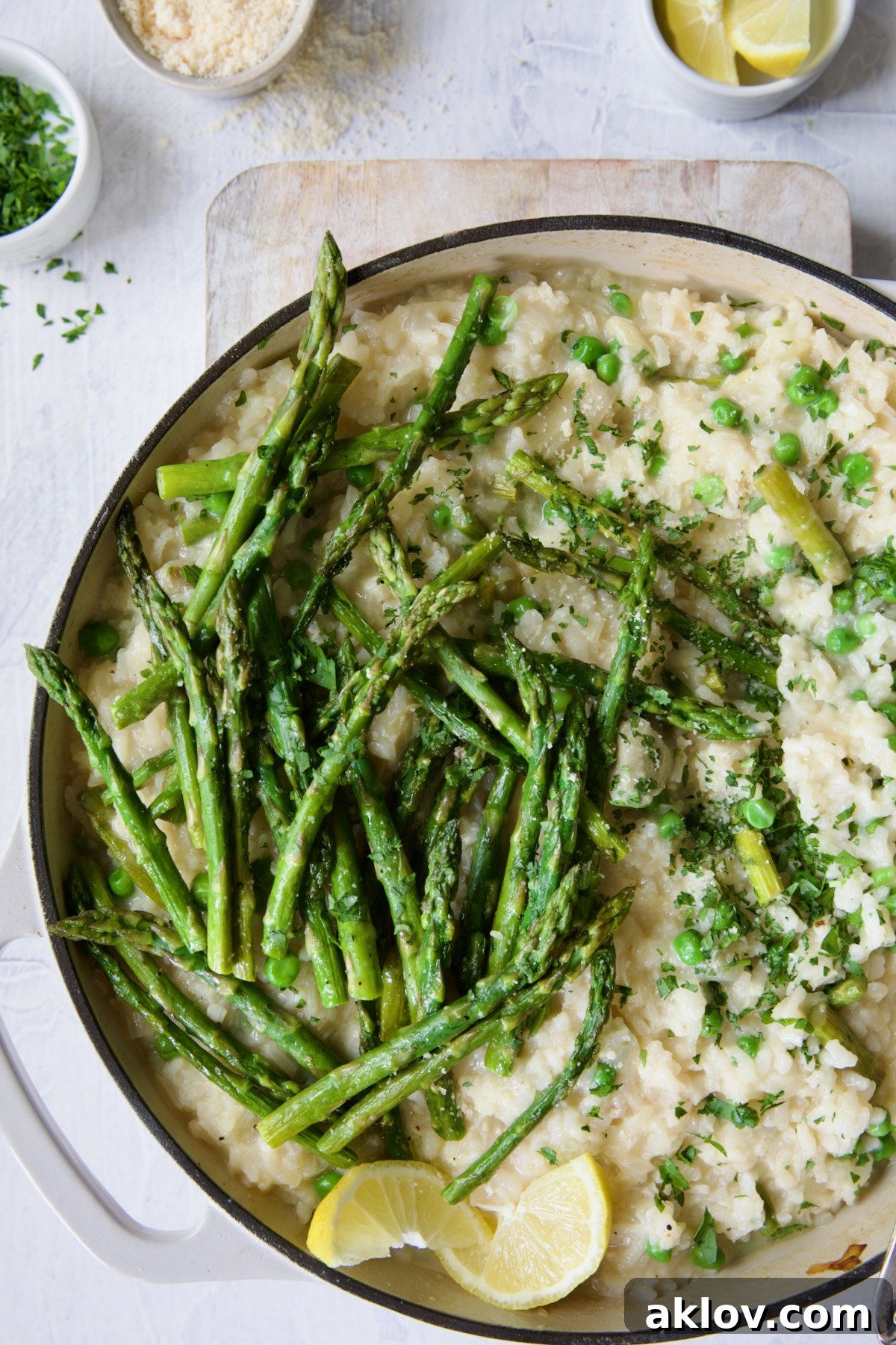 Finished risotto with asparagus tips in white enamel cast iron skillet garnished with lemon wedges.