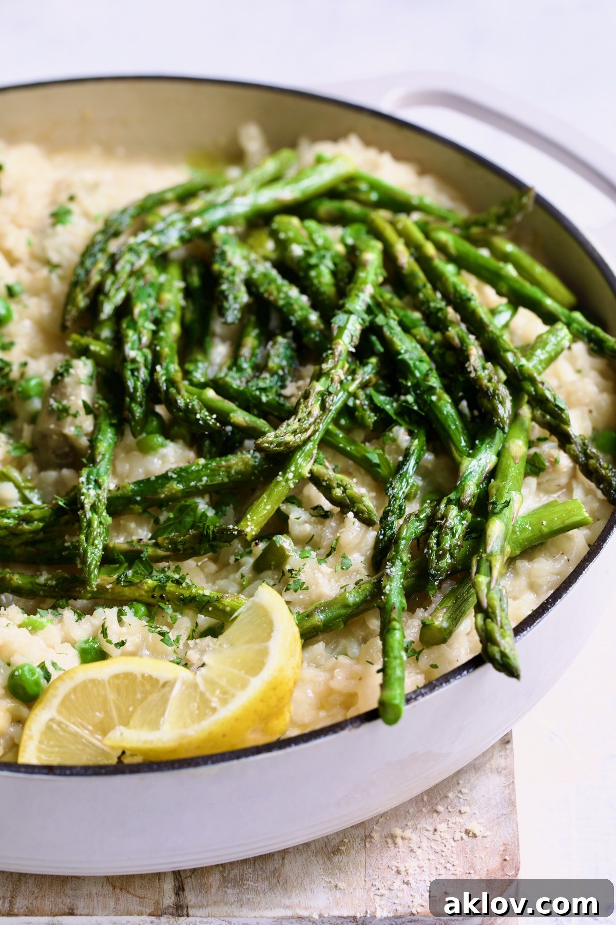 Finished risotto with asparagus tips in white enamel cast iron skillet garnished with lemon wedges.