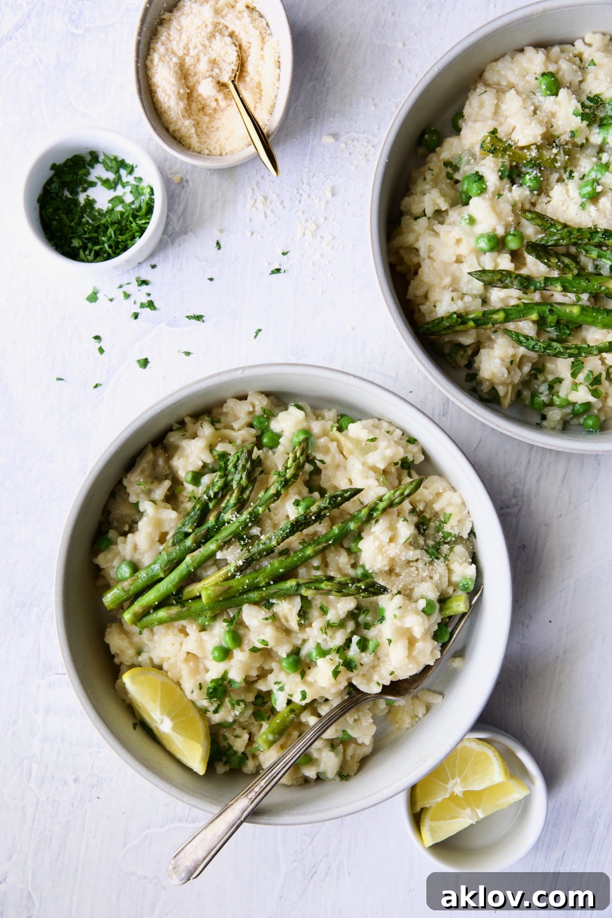 Two bowls of Easy Risotto Recipe with Spring Vegetables garnished with asparagus spears and lemon wedge.