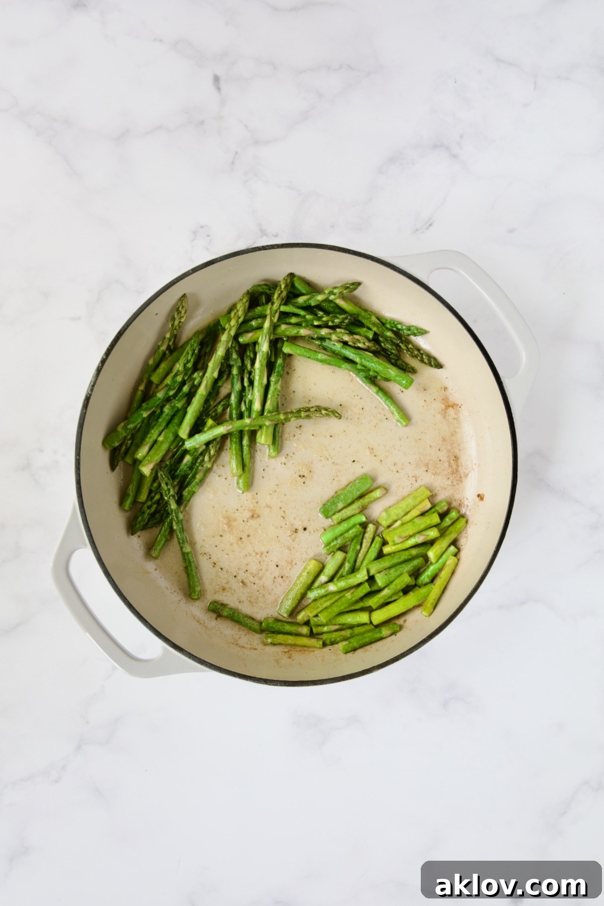 Asparagus tips and stems in white enamel cast iron skillet.