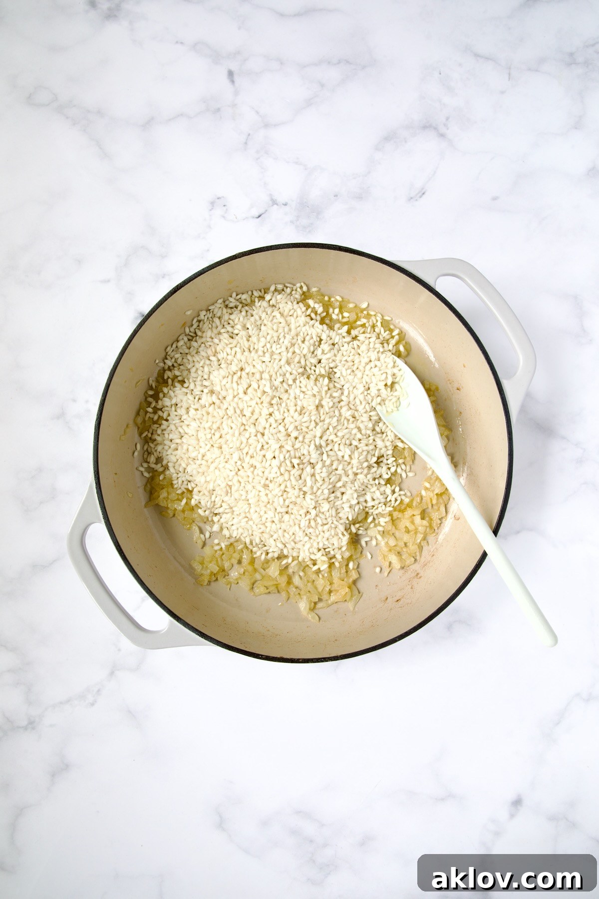 Arborio rice added to onions and garlic in white enamel cast iron skillet.