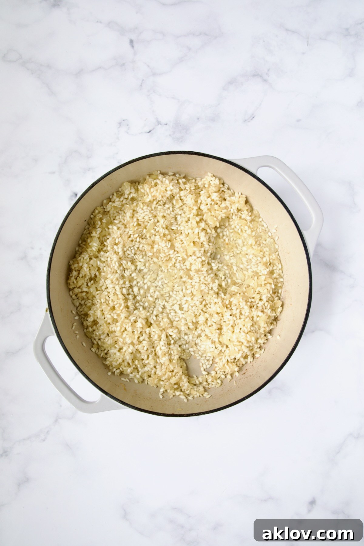 Wine added to rice, onions and garlic in white enamel cast iron skillet.