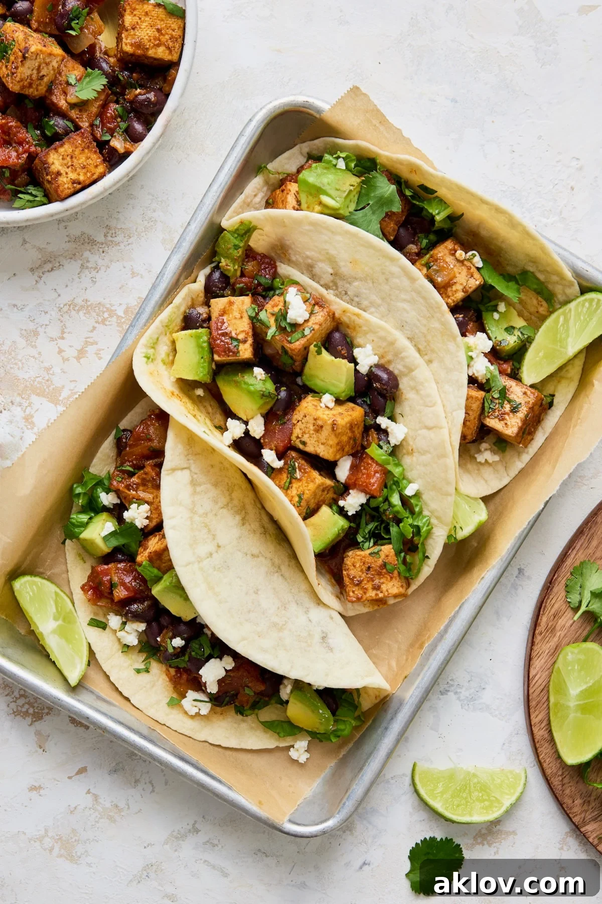 Three Tofu Black Bean Tacos elegantly arranged on an aluminum pan, garnished with fresh lime wedges and vibrant cilantro.