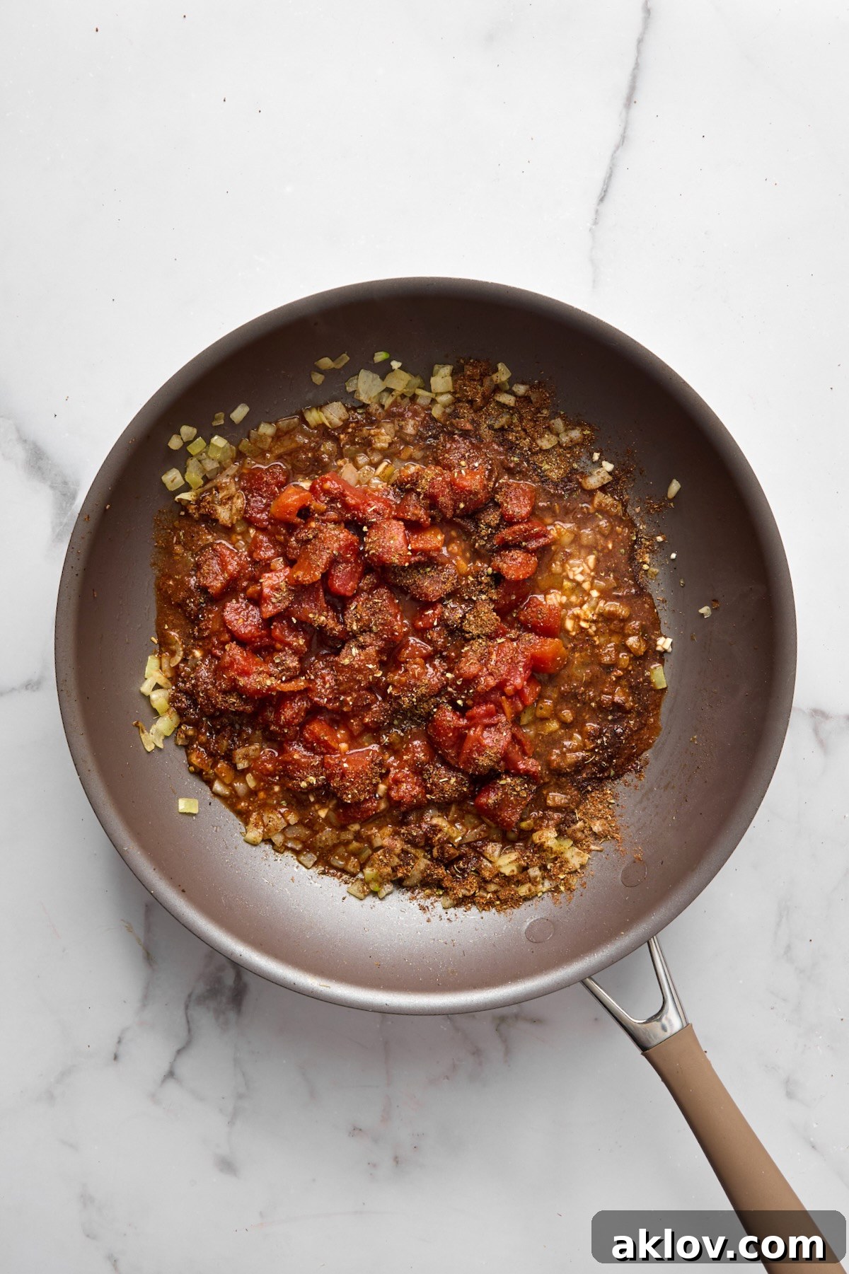 Diced tomatoes, minced garlic, and the remaining spice blend added to the softened onions in the nonstick skillet, simmering to meld flavors.