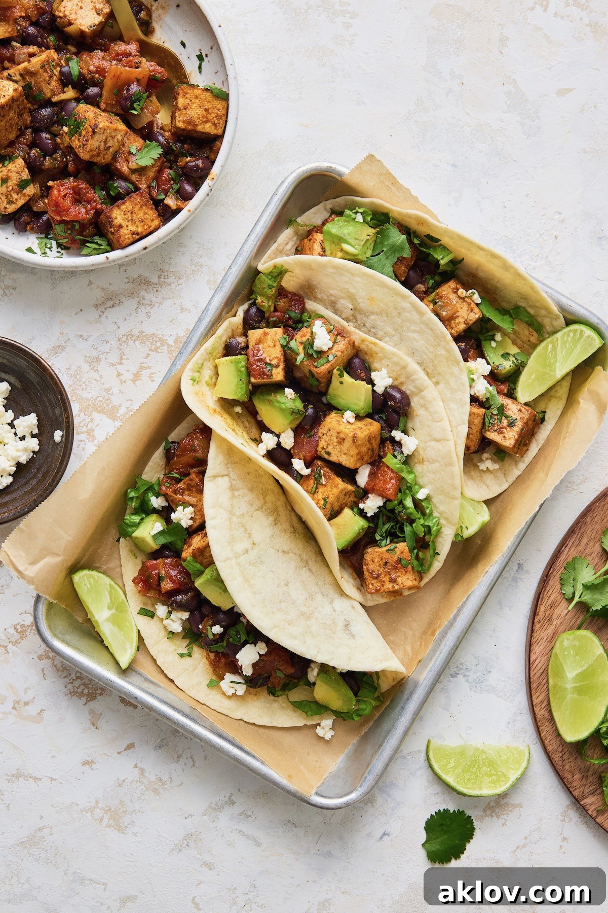 Three perfectly assembled Tofu Black Bean Tacos on an aluminum pan, garnished with lime wedges and ready to be served.