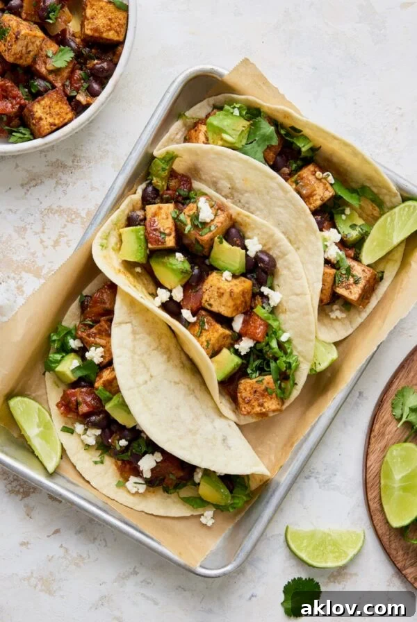 Three Tofu Black Bean Tacos on aluminum pan garnished with lime wedges.
