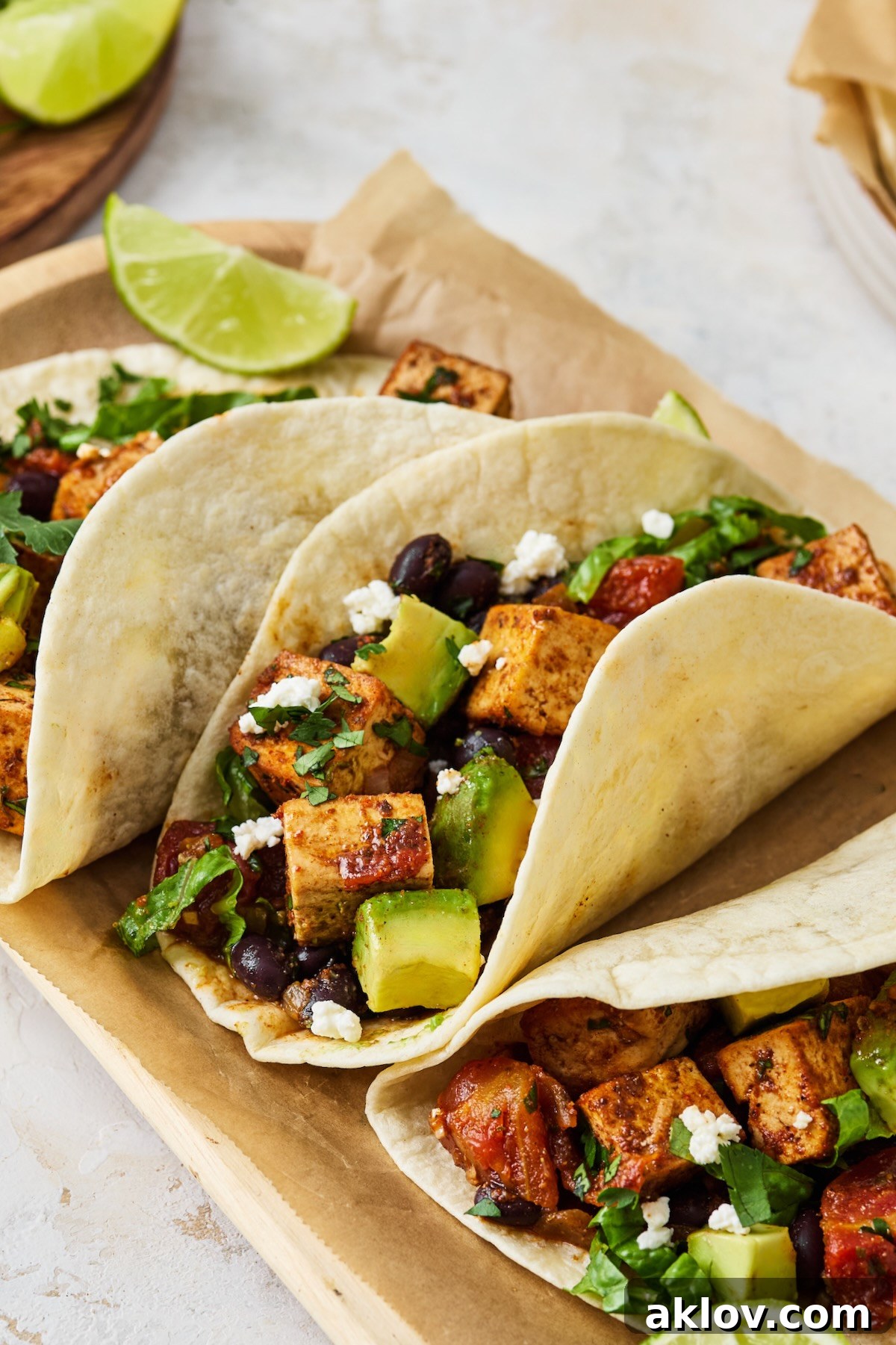Three Tofu Black Bean Tacos presented on parchment paper within a rustic wooden tray, ready to be enjoyed.