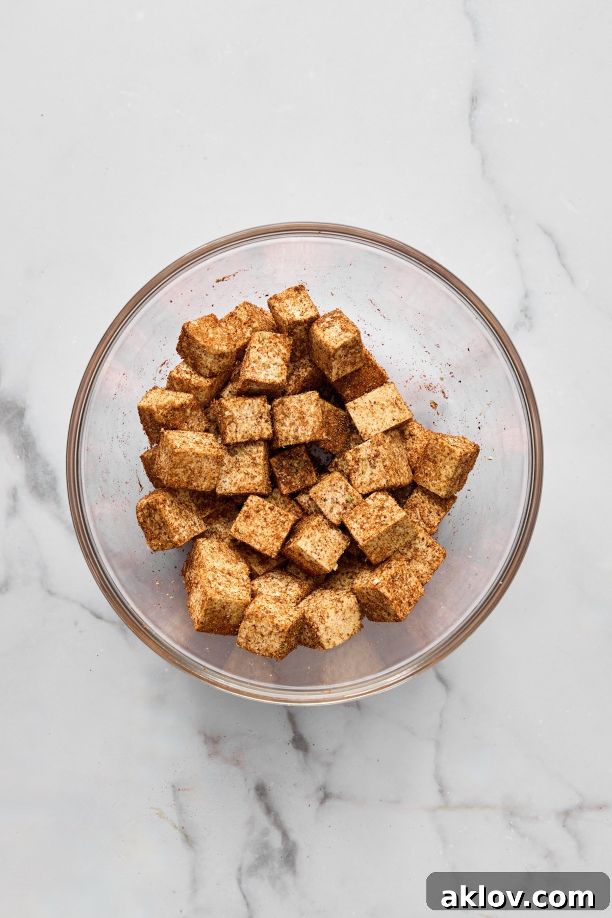 Tofu cubes generously coated with a savory spice blend in a glass bowl, ready for pan-searing.