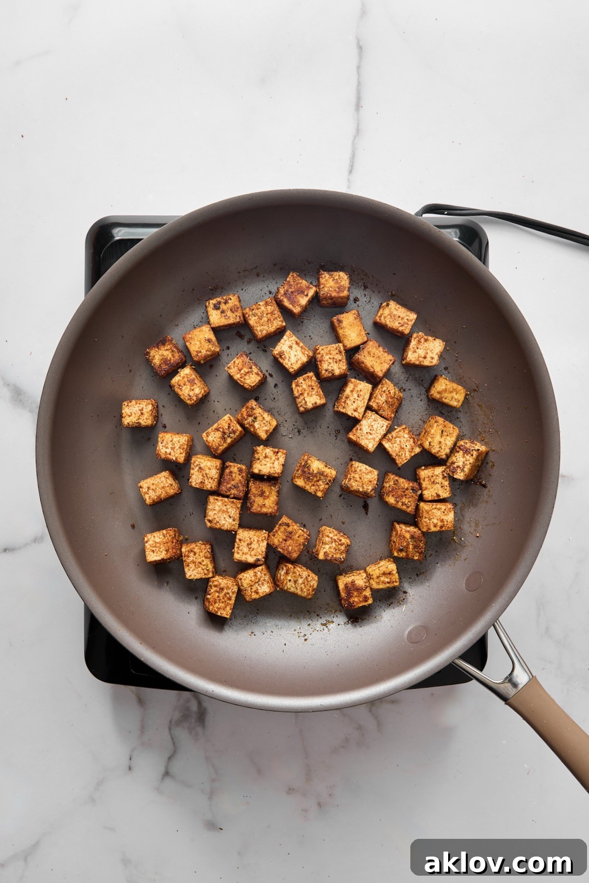 Seasoned tofu cubes sizzling and browning in a nonstick skillet over medium-high heat.