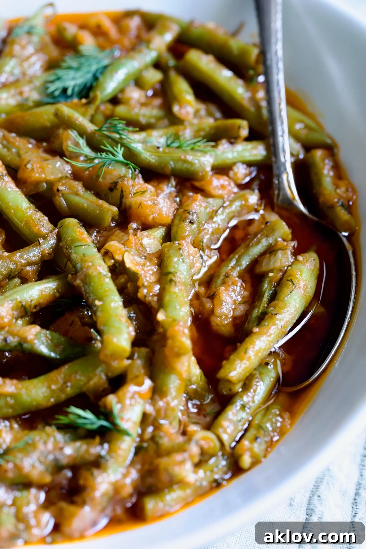 Greek Green Beans in a white bowl with a serving spoon, garnished with fresh dill.