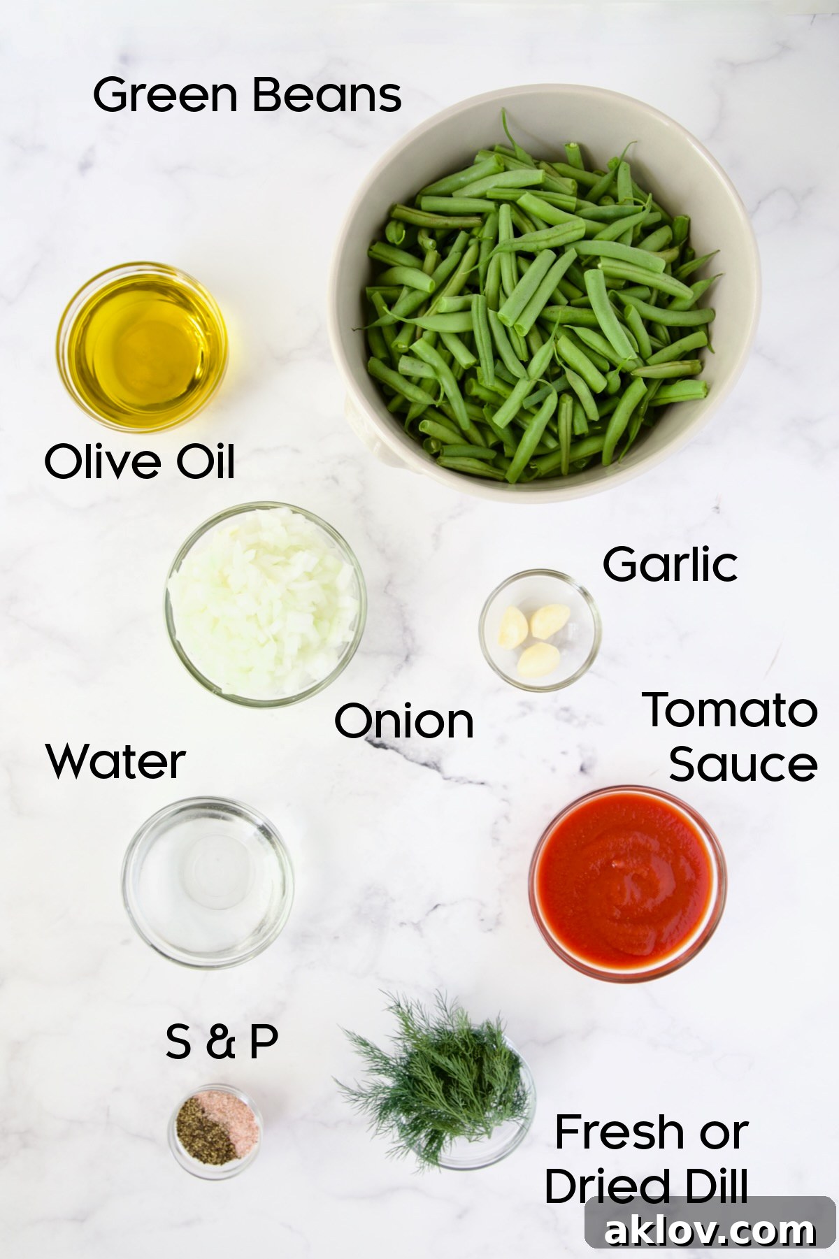 A selection of fresh ingredients for Greek Green Beans, including green beans, tomatoes, dill, and garlic, arranged in bowls on a countertop.