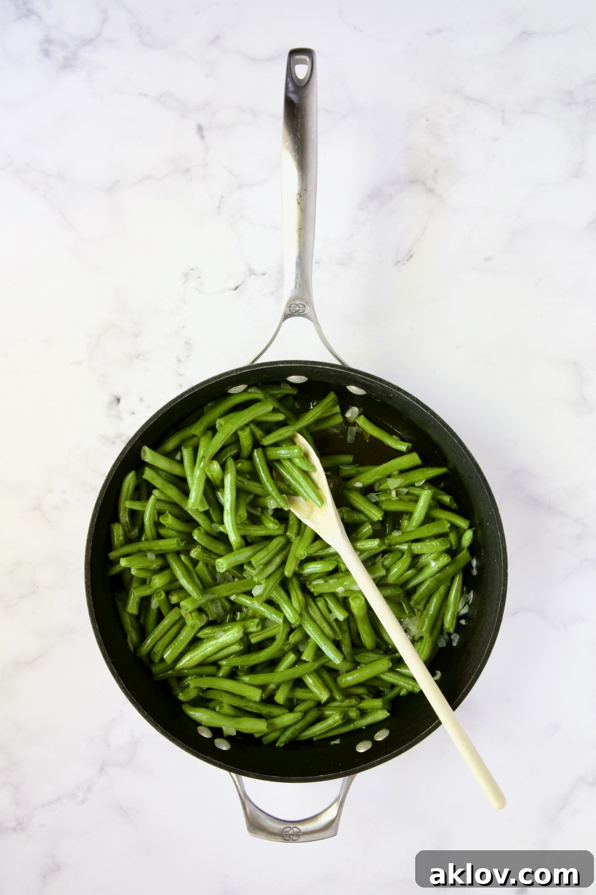 Green beans being tossed and sauteed with onions and garlic in a nonstick skillet.
