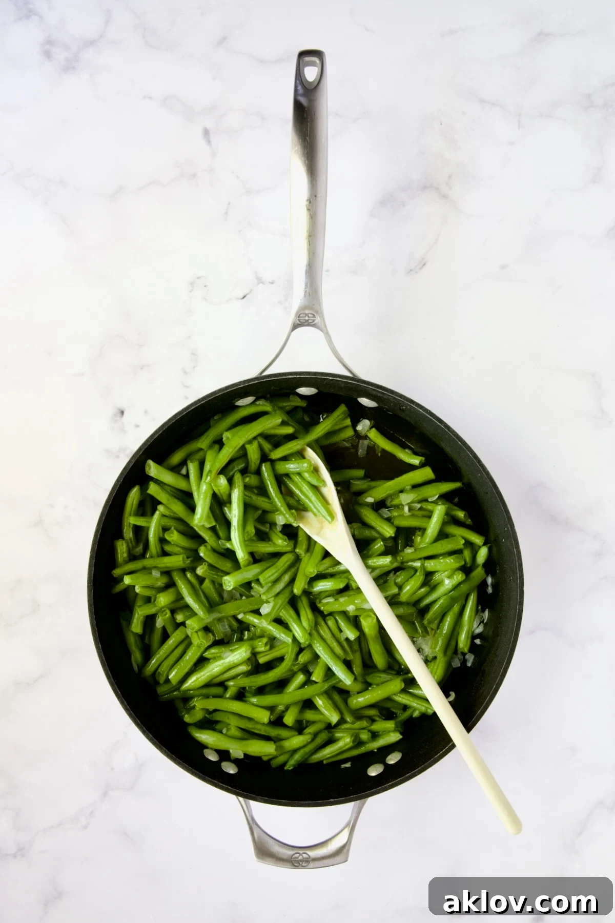 Green beans being sauteed with onions and garlic in a nonstick skillet.