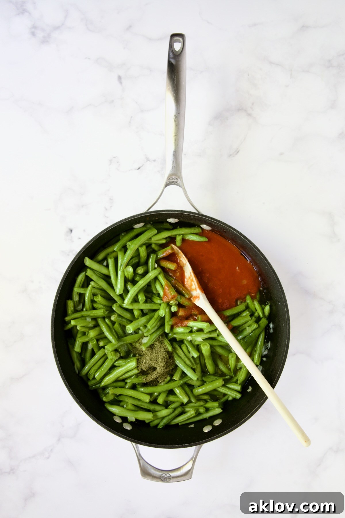 Green beans simmering with tomato sauce and dried dill in a nonstick skillet.