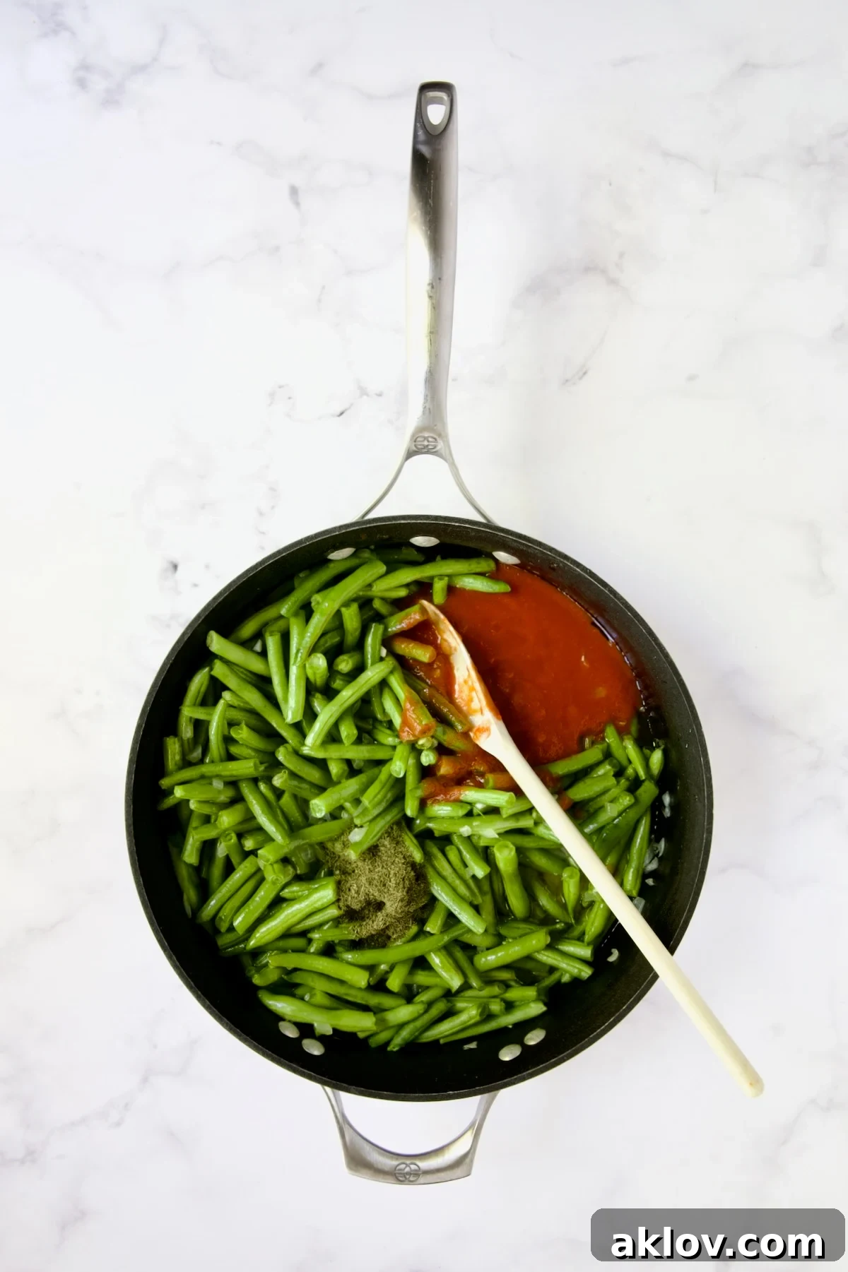 Green beans in a nonstick skillet covered with tomato sauce and dried dill.