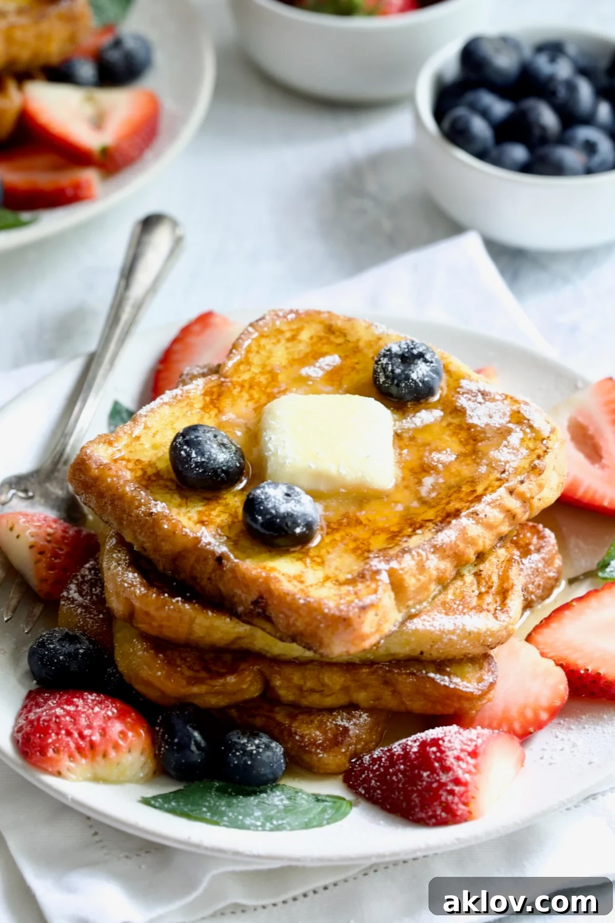 Decadent Brioche French Toast on a white plate, topped with a pat of butter, fresh blueberries, and sliced strawberries, ready to be served.