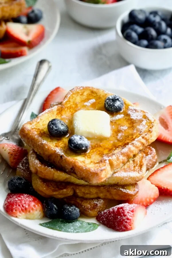 Brioche French Toast on a white plate, topped with a pat of butter, fresh blueberries, and sliced strawberries.
