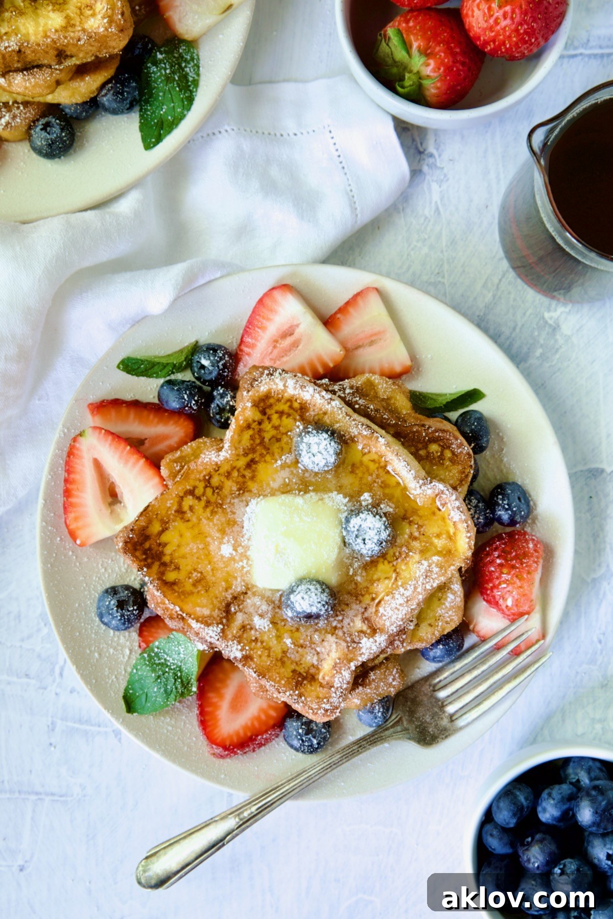 Close-up of golden-brown Brioche French Toast slices stacked on a white plate.