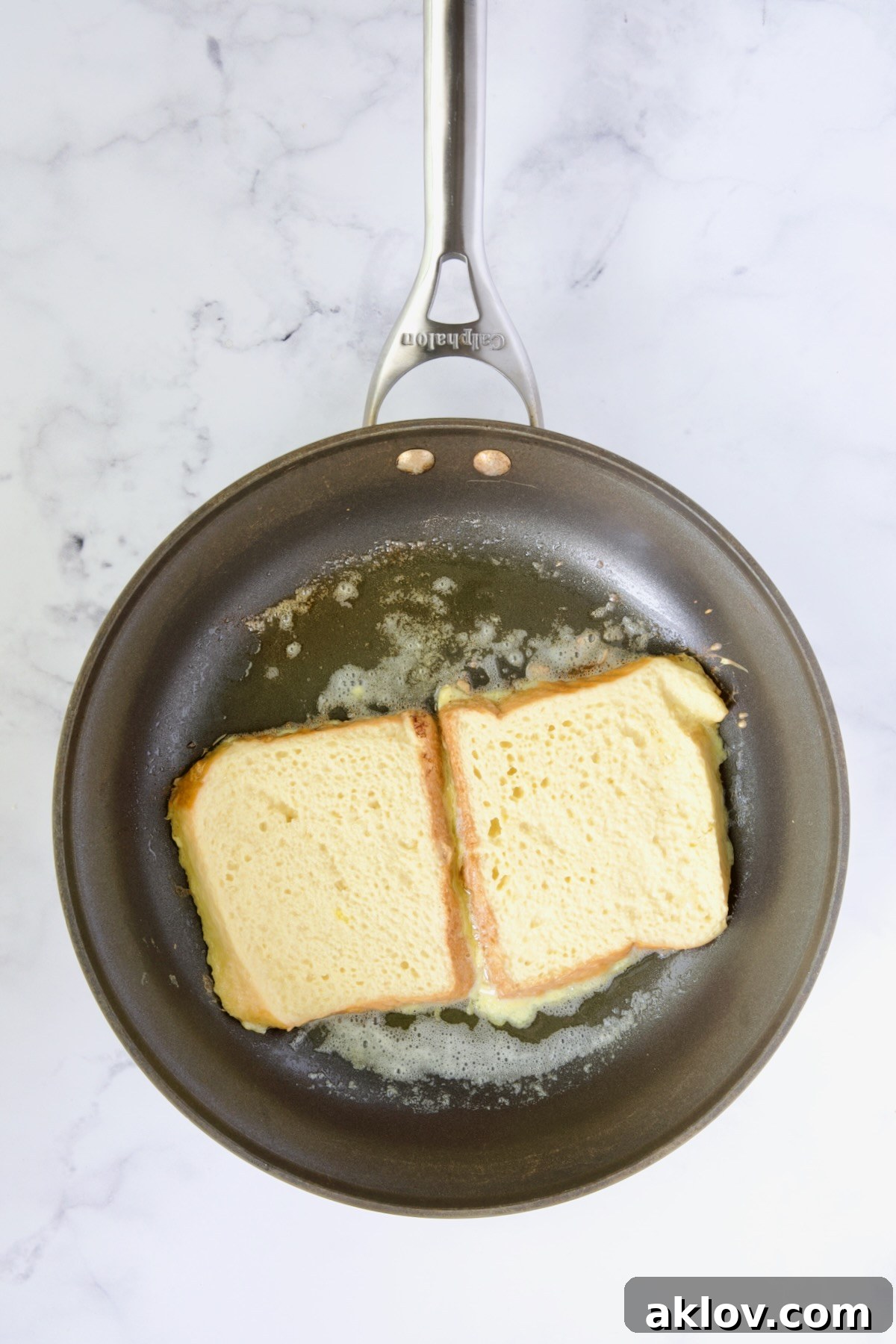 Two slices of Brioche French Toast cooking in a nonstick skillet, beautifully browning on the first side.