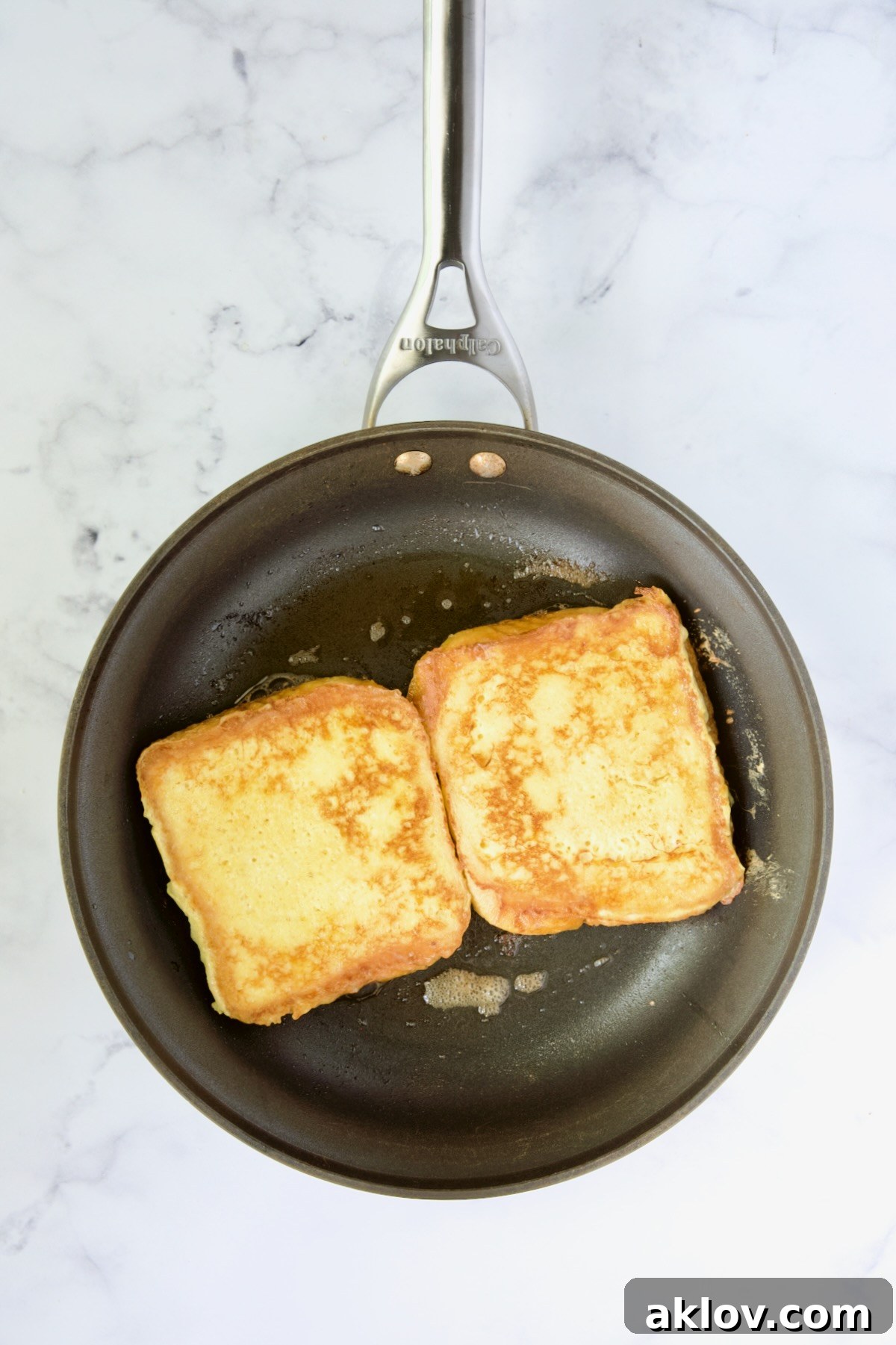 Two slices of Brioche French Toast flipped and cooking on the second side in a nonstick skillet, achieving a perfect golden color.