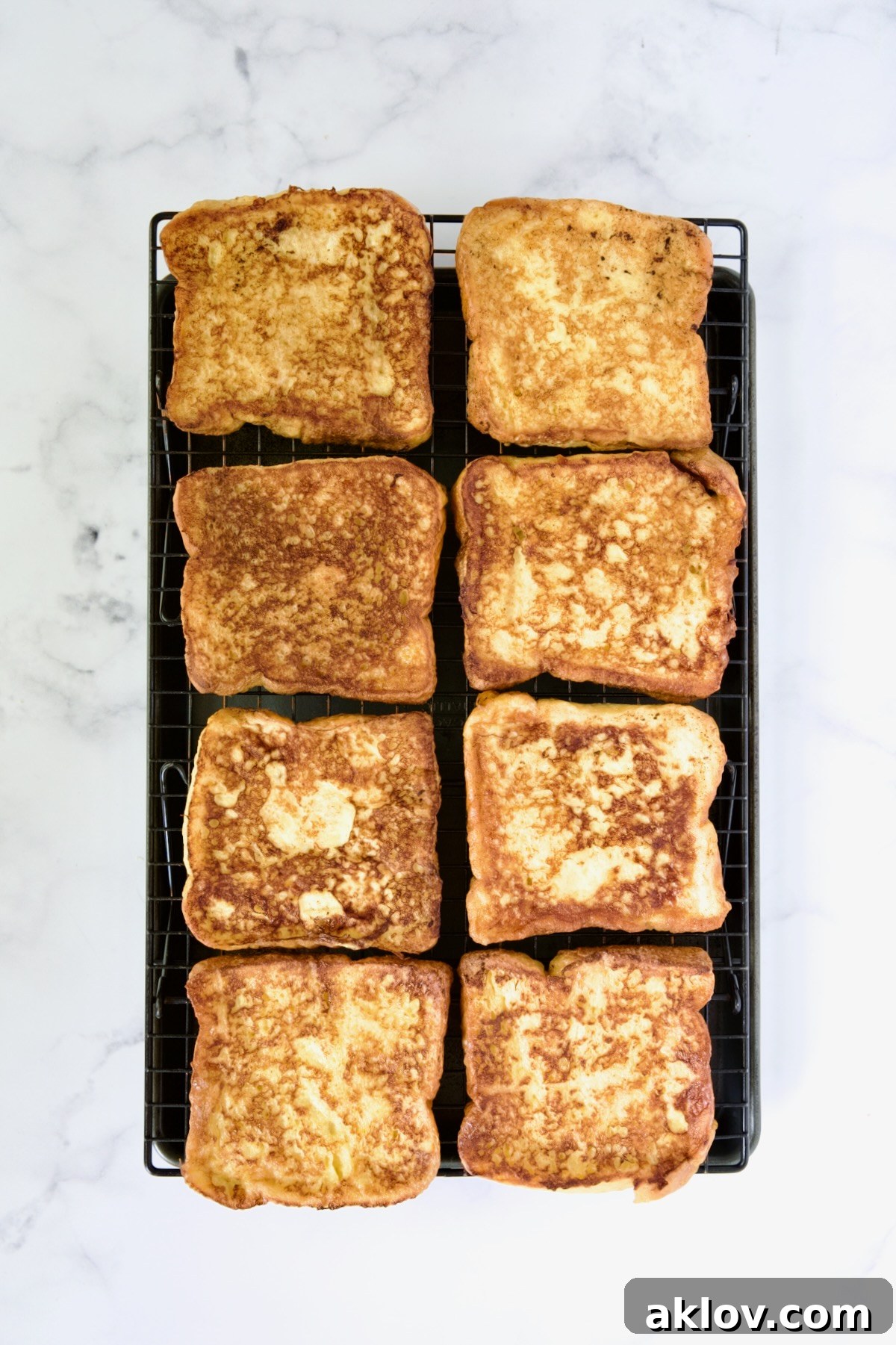 Eight slices of perfectly cooked Brioche French Toast neatly arranged on a cooling rack set over a rimmed sheet pan, kept warm in the oven.