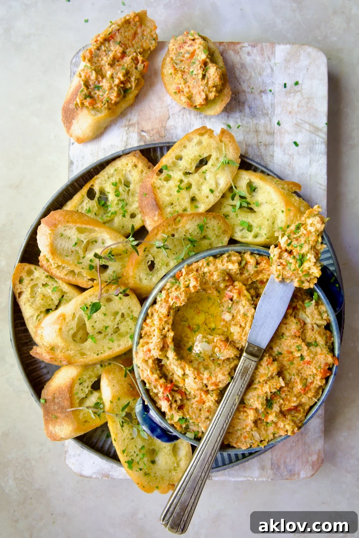 Artichoke Tapenade with Crostini on whitewashed board, garnished with fresh herbs.