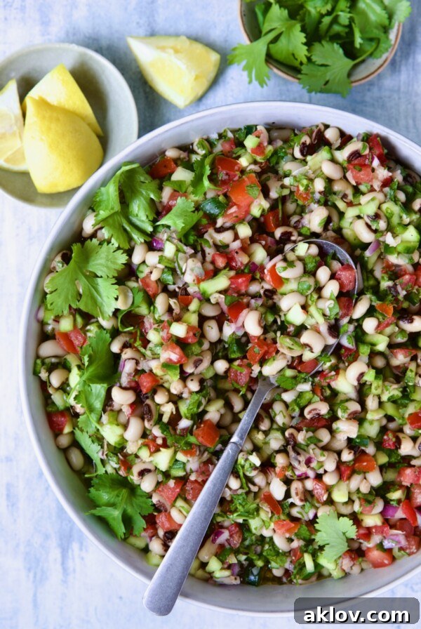 Black-Eyed Pea Salad in white bowl with lemon wedges and cilantro in bowls.