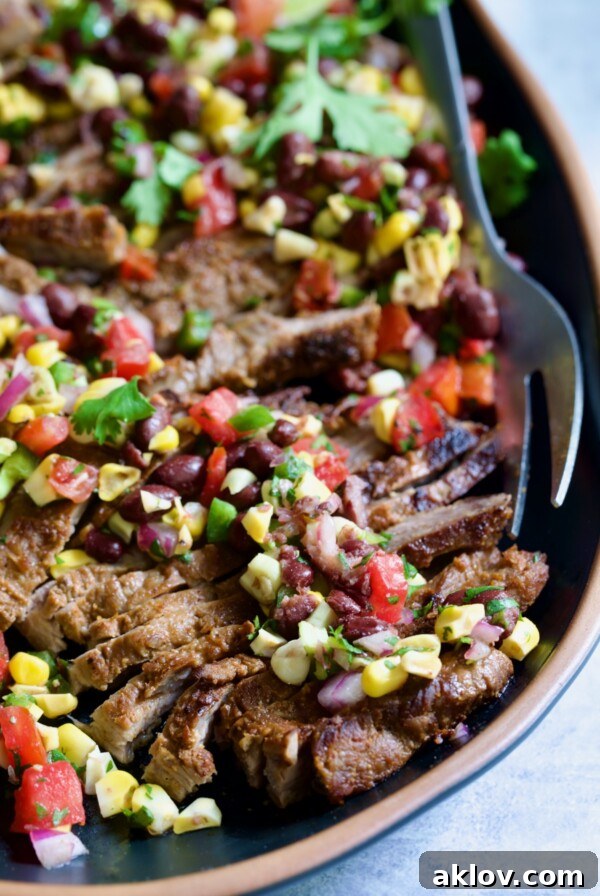 Grilled Skirt Steak with Black Bean Tomato Corn Salad on black platter with serving fork.